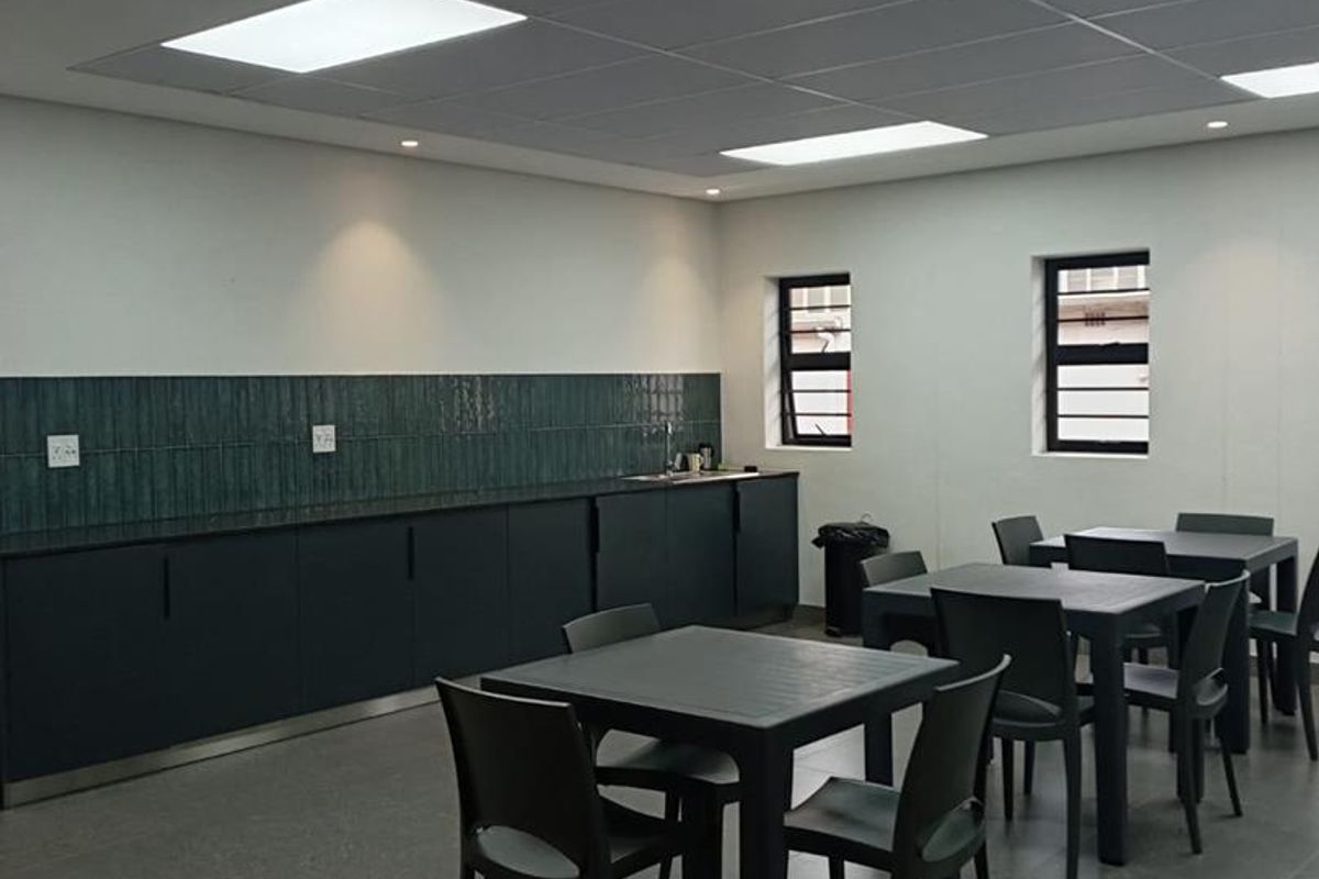 A clean, modern industrial kitchen area featuring dark cabinetry, a tiled backsplash, and recessed lighting, suitable for office or commercial use.