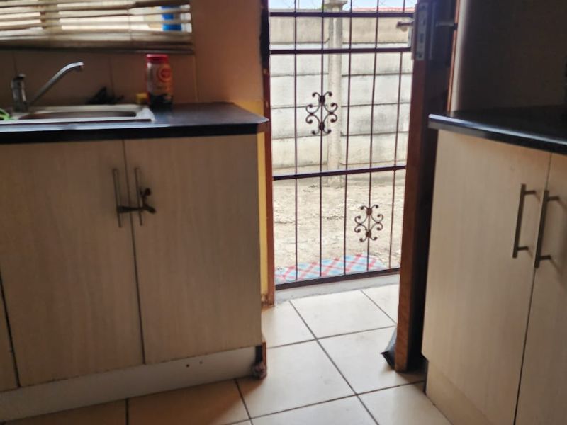 A compact kitchen area featuring laminate cabinetry, dark countertops, and a stainless steel sink, with direct access to an outdoor area via a security gate.