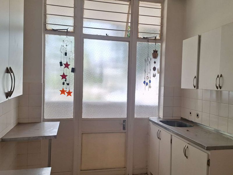 A functional kitchen space featuring built-in cabinetry, a stainless steel sink, and tiled backsplash, offering a blank canvas for modern renovation.