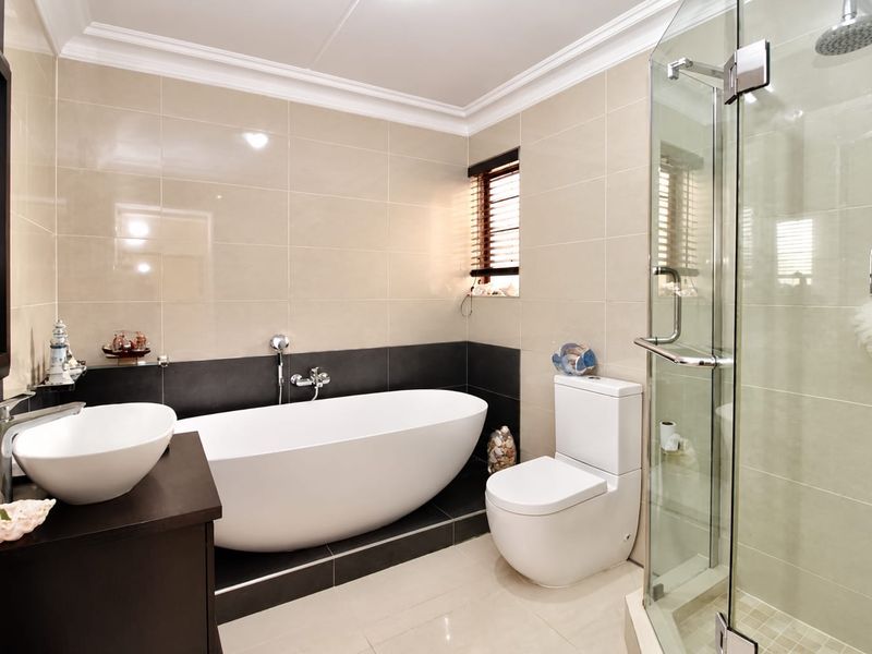 Modern bathroom featuring a sleek freestanding bathtub, separate glass-enclosed shower, contemporary vanity basin, and neutral floor-to-ceiling tiling.
