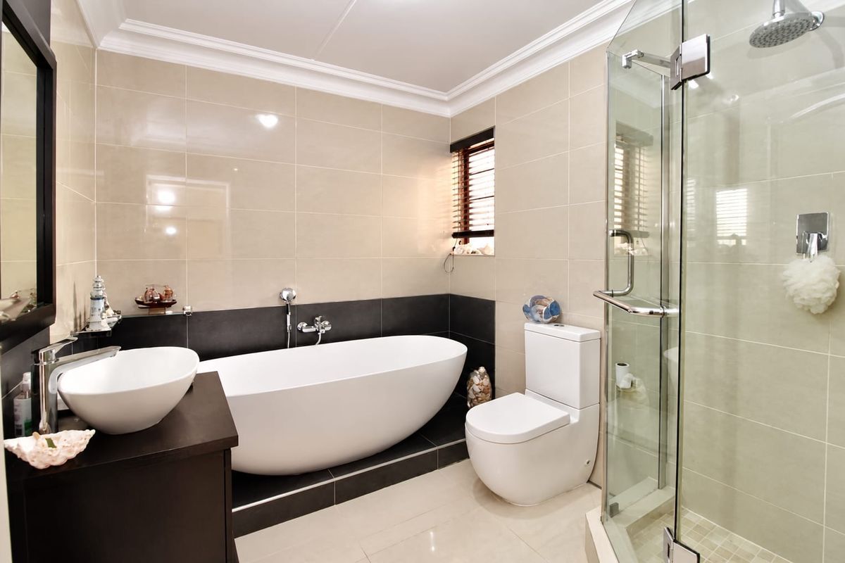 Modern bathroom featuring a sleek freestanding bathtub, separate glass-enclosed shower, contemporary vanity basin, and neutral floor-to-ceiling tiling.