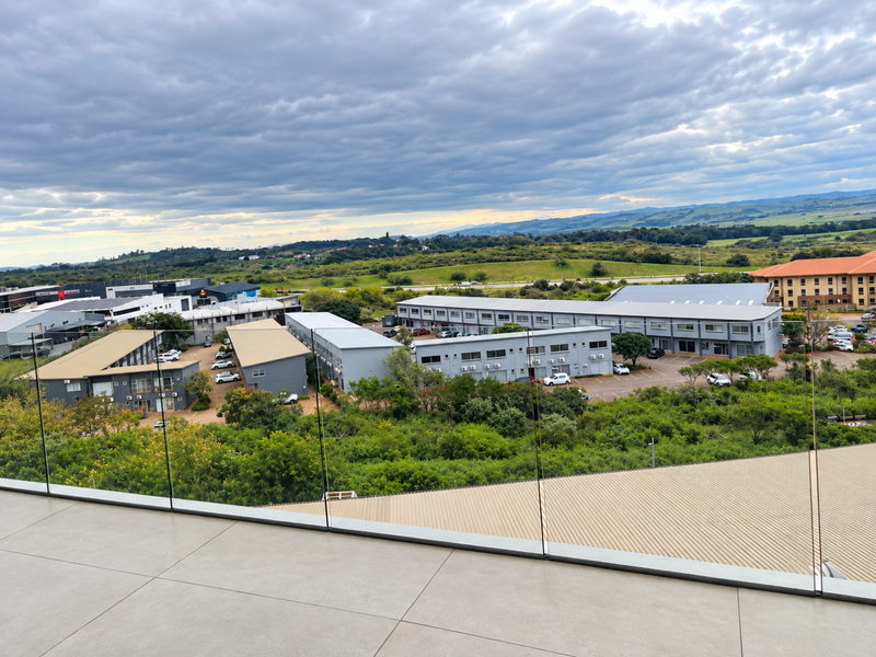 Elevated aerial view overlooking a commercial business park complex with surrounding greenery and distant landscape under a cloudy sky.