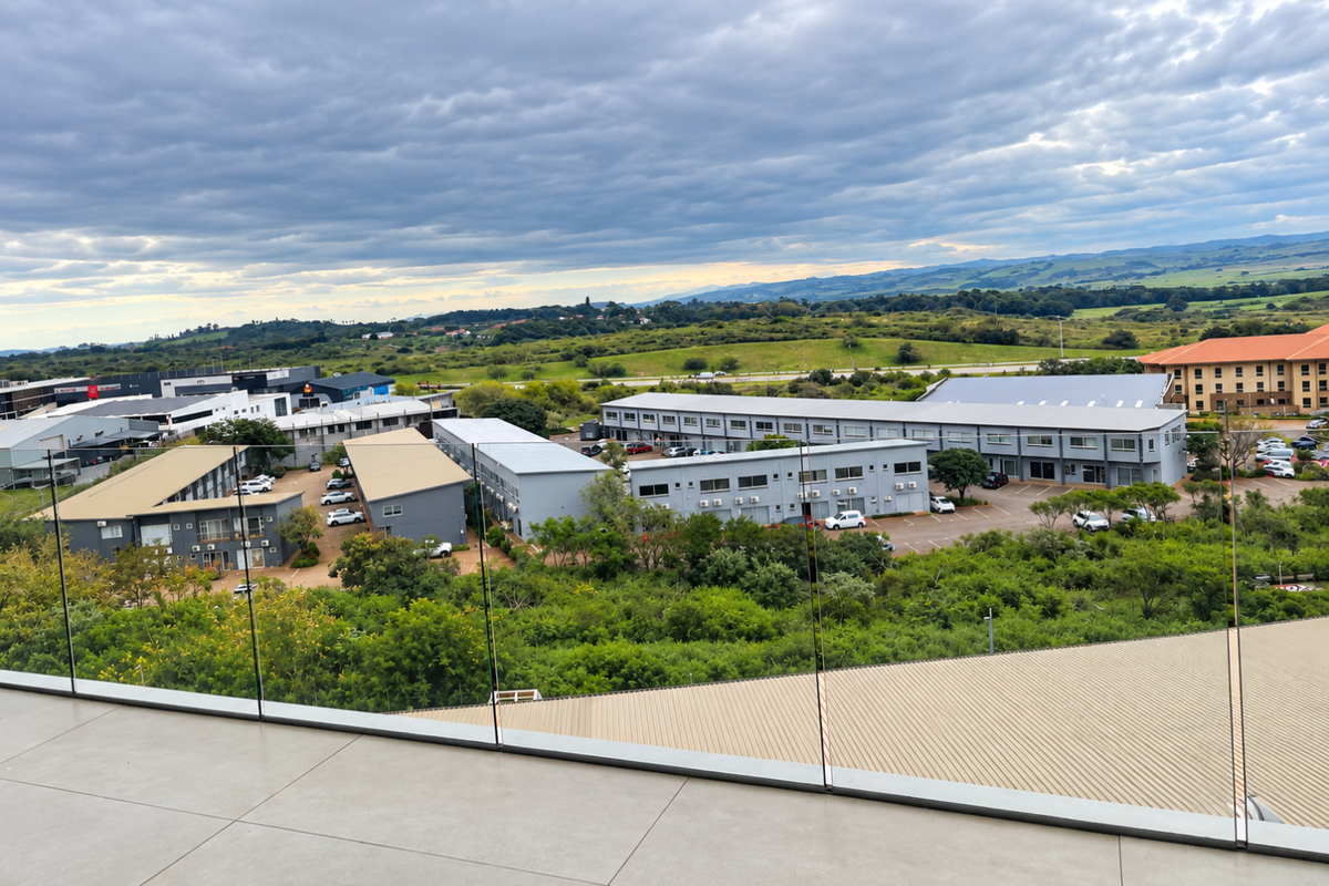 Elevated aerial view overlooking a commercial business park complex with surrounding greenery and distant landscape under a cloudy sky.