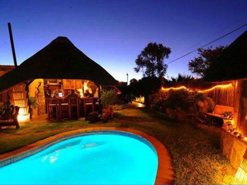 An inviting outdoor pool area featuring a thatched lapa with a built-in bar, perfect for evening entertainment and relaxation.