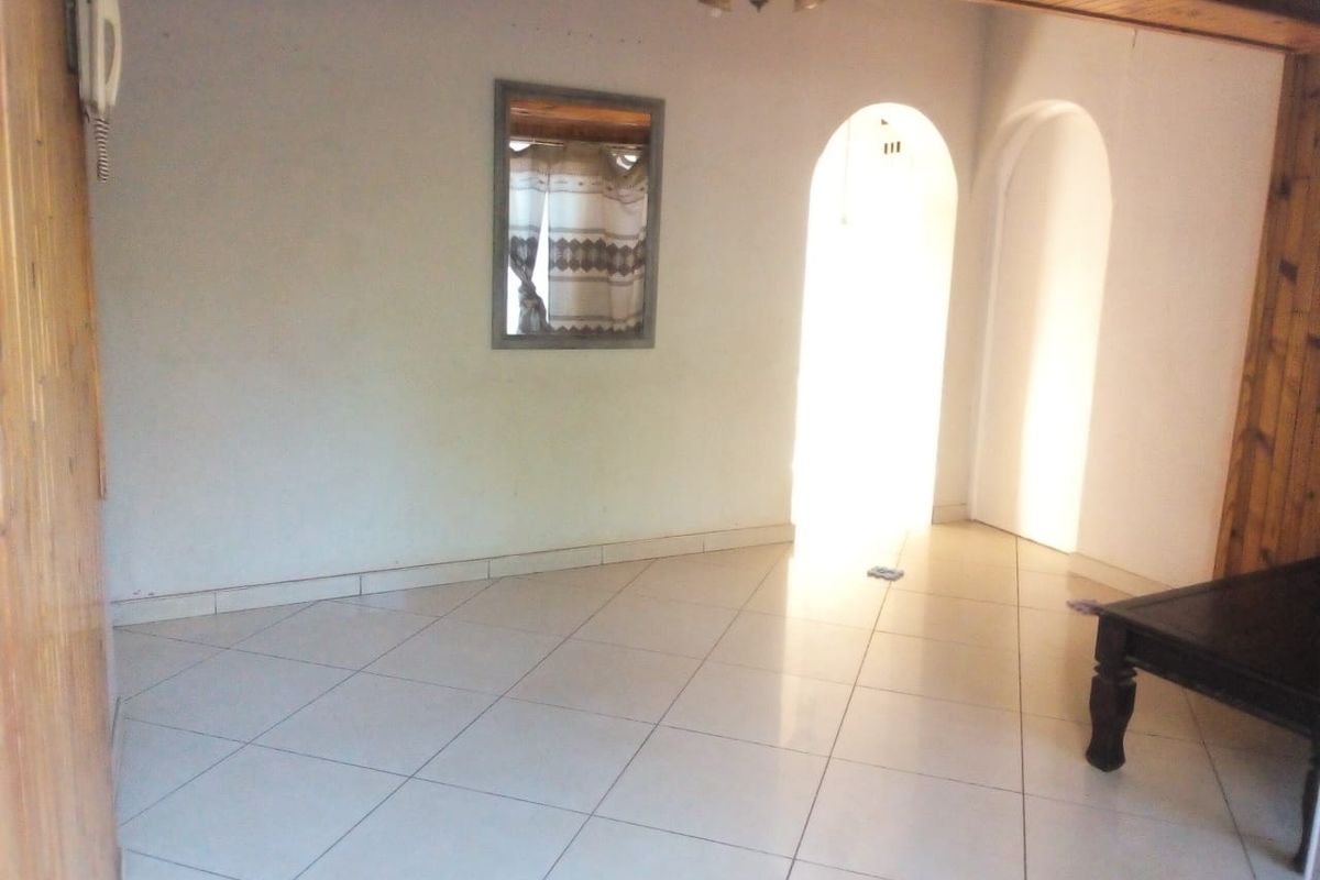 A bright, open living area featuring tiled flooring, timber ceiling accents, and distinctive arched doorways leading to adjacent rooms.