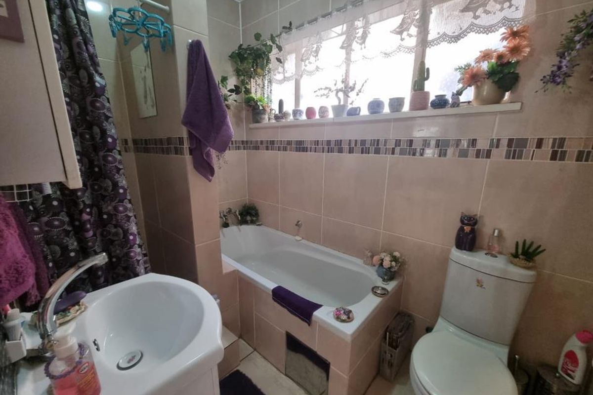 A functional bathroom featuring a built-in bathtub, a pedestal sink, and a standard toilet with tiled walls and a window.
