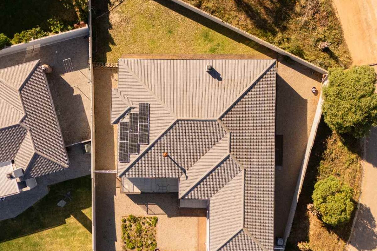 Aerial view of the property showing the tiled roof, integrated solar panels, and surrounding landscaped garden area.