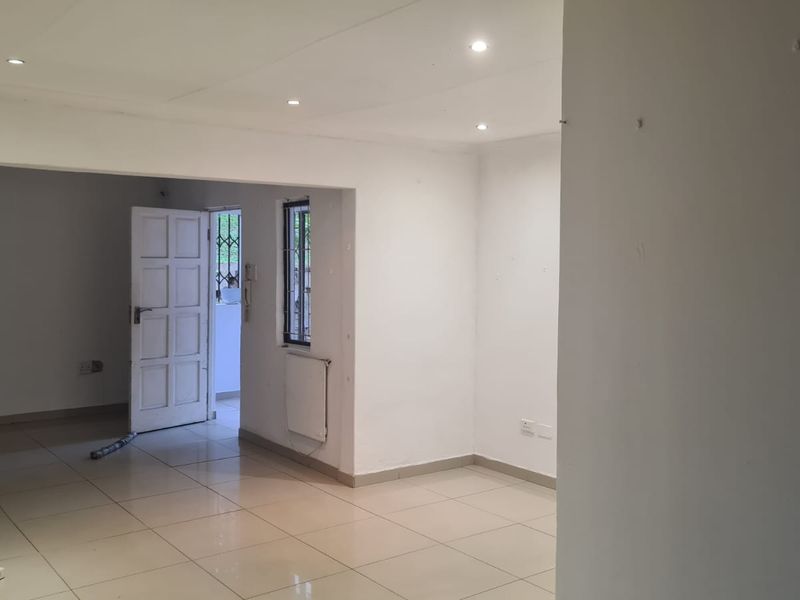An empty, open-plan living area featuring neutral tiled flooring, recessed downlighting, and a wall-mounted heater, providing a blank canvas for interior design.