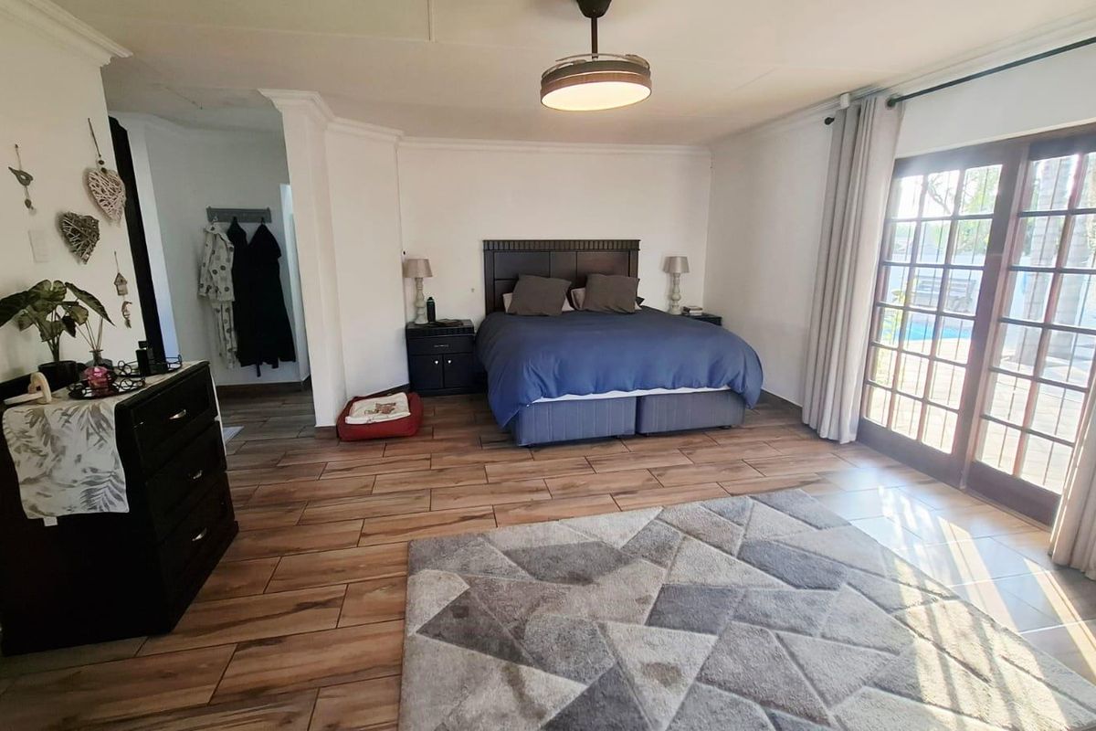 Spacious bedroom featuring wood-look tiled flooring, a ceiling light fixture, and direct access to the outdoor area through glass-paned french doors.