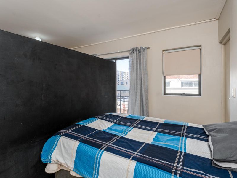 A bedroom featuring a large black partition wall, a window with a roller blind, and a sliding glass door leading to an outdoor area.