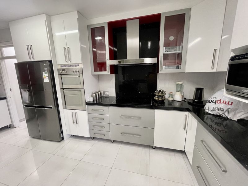 Modern kitchen featuring high-gloss cabinetry, granite countertops, built-in oven, and a sleek extractor fan with a contrasting black splashback.