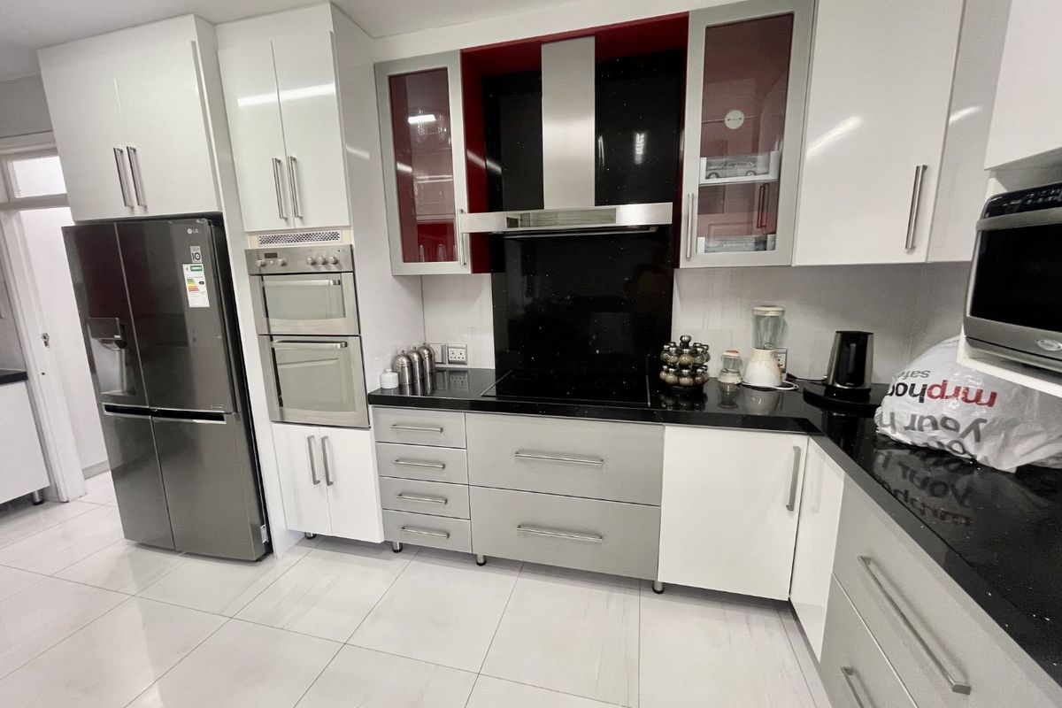 Modern kitchen featuring high-gloss cabinetry, granite countertops, built-in oven, and a sleek extractor fan with a contrasting black splashback.