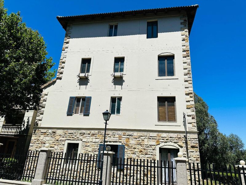 A multi-story apartment building facade featuring stone masonry detailing, traditional shutters, and a secure wrought iron perimeter fence.