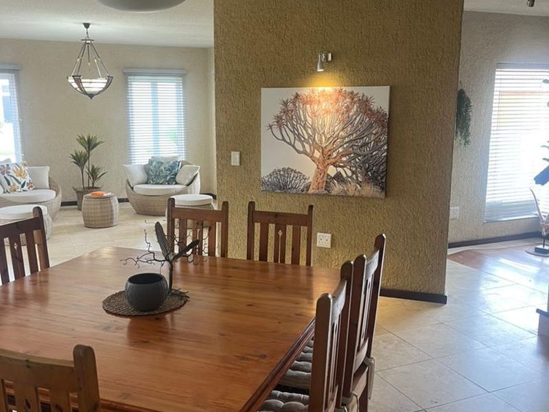 Spacious open-plan dining and living area featuring tiled floors, a textured feature wall, and ample natural light through venetian blinds.
