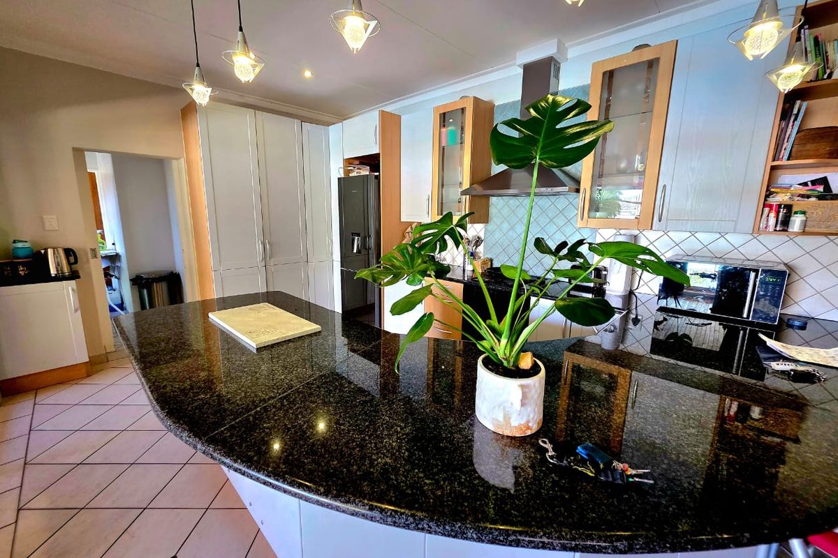 A well-appointed kitchen featuring granite countertops, ample built-in cabinetry, stainless steel extractor fan, and modern pendant lighting over a spacious breakfast bar.