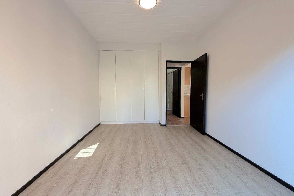 A bright, empty bedroom featuring modern light-toned laminate flooring and white built-in cupboards, offering a clean and neutral space ready for personalization.