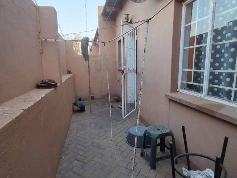 A narrow rear courtyard featuring paved flooring, an external electric water heater, and security features including burglar bars and a perimeter wall.