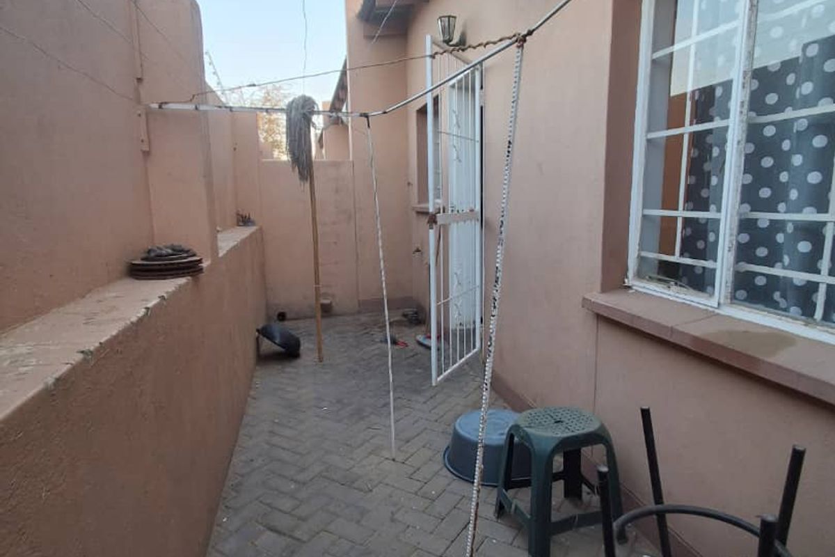A narrow rear courtyard featuring paved flooring, an external electric water heater, and security features including burglar bars and a perimeter wall.