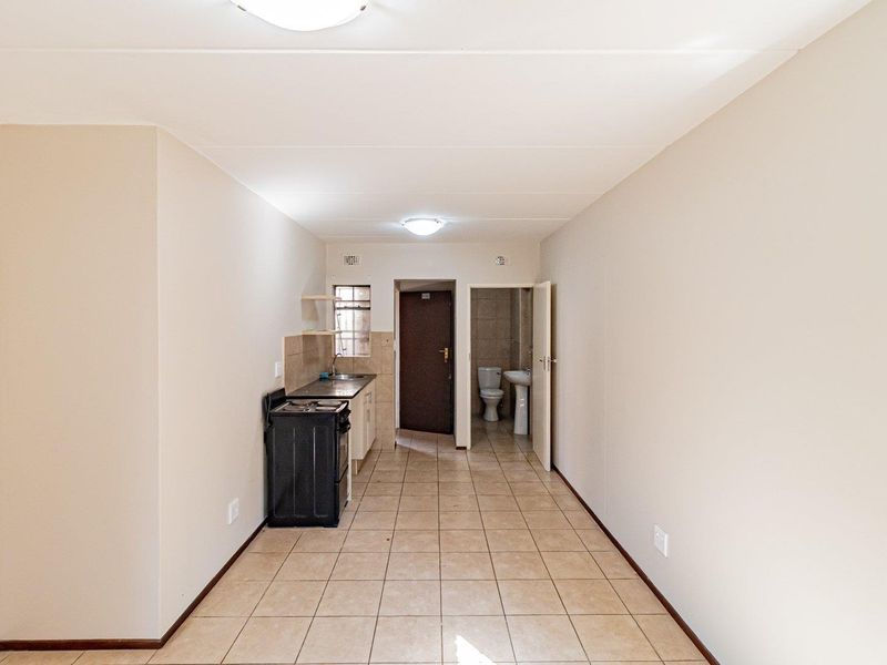 An open-plan living area featuring tiled flooring, a compact kitchen with cabinetry and stove, and direct access to an adjacent bathroom.