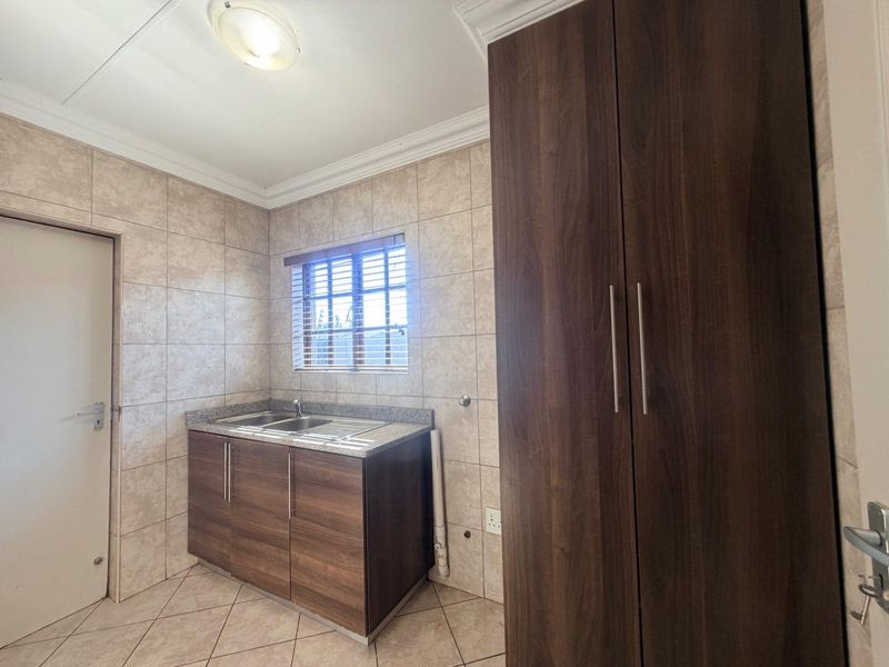 A clean and functional laundry room featuring built-in dark wood cabinetry, a stainless steel sink, tiled walls, and tiled flooring.