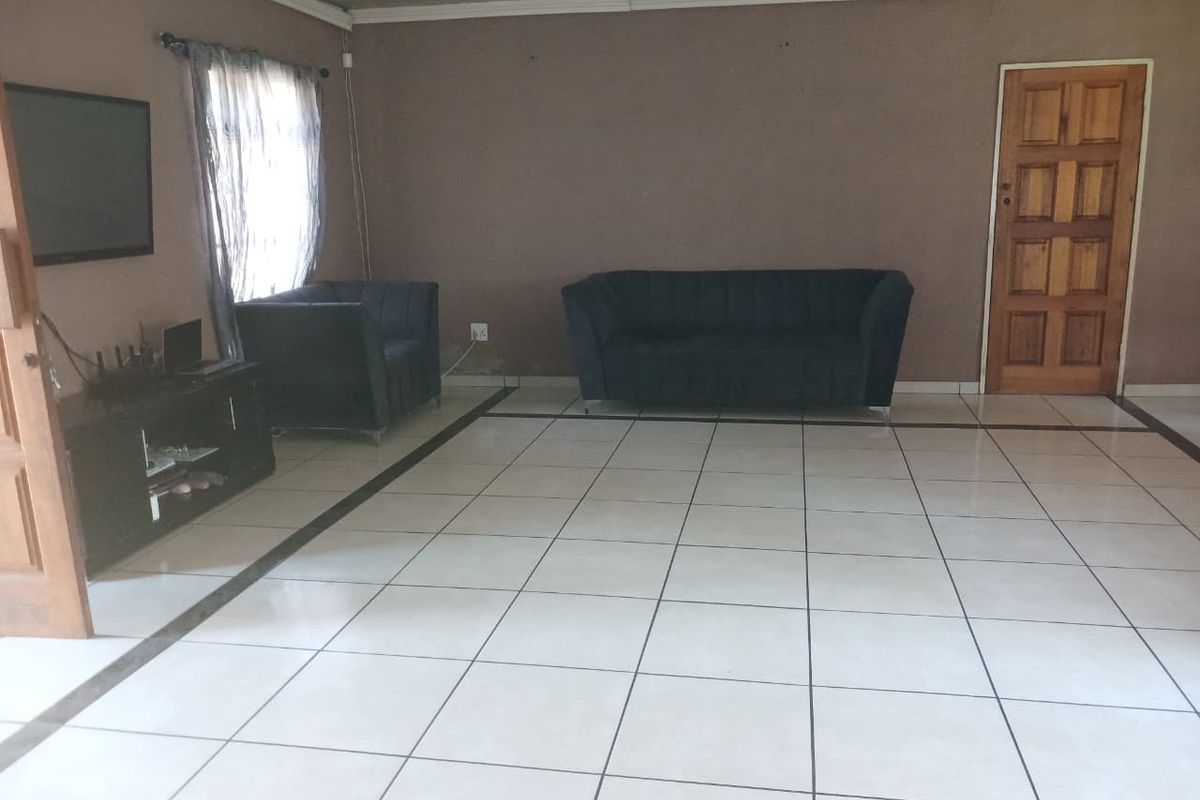 A spacious living room featuring large white floor tiles, a wooden entrance door, and neutral wall tones, offering a blank canvas for interior design.