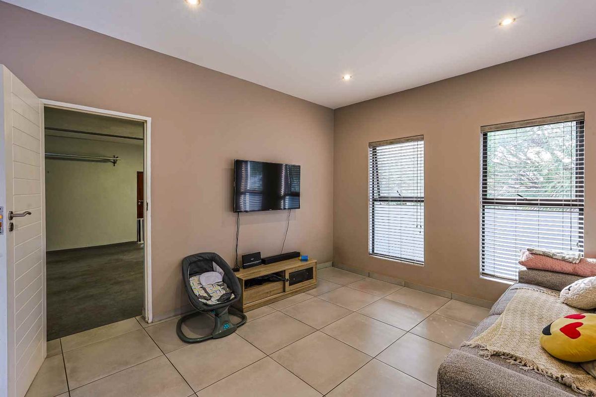 A living room featuring neutral wall tones, tiled flooring, recessed downlighting, and two windows fitted with horizontal blinds.