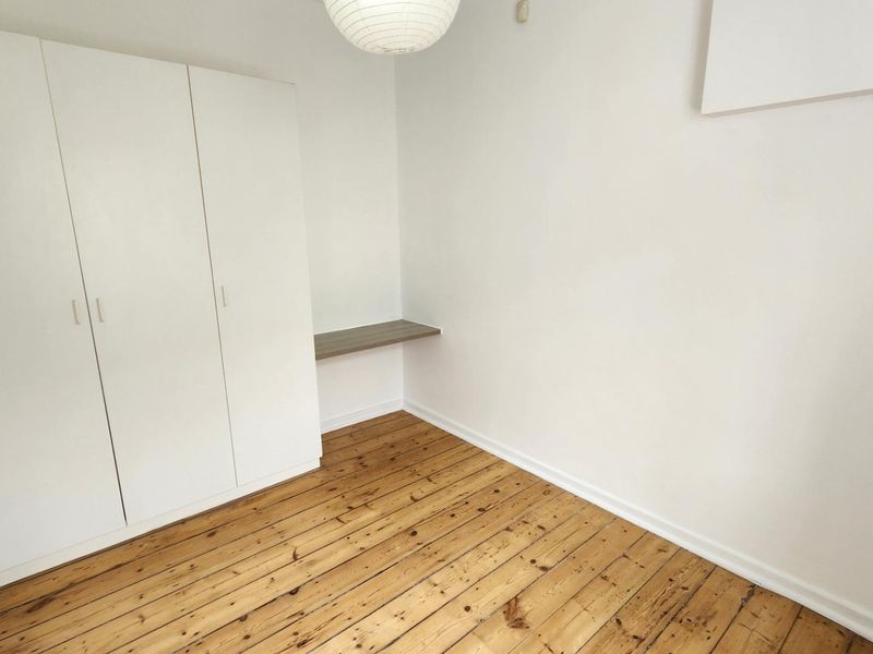 A bright, empty bedroom featuring polished timber flooring, a built-in wardrobe, and a convenient floating desk shelf.