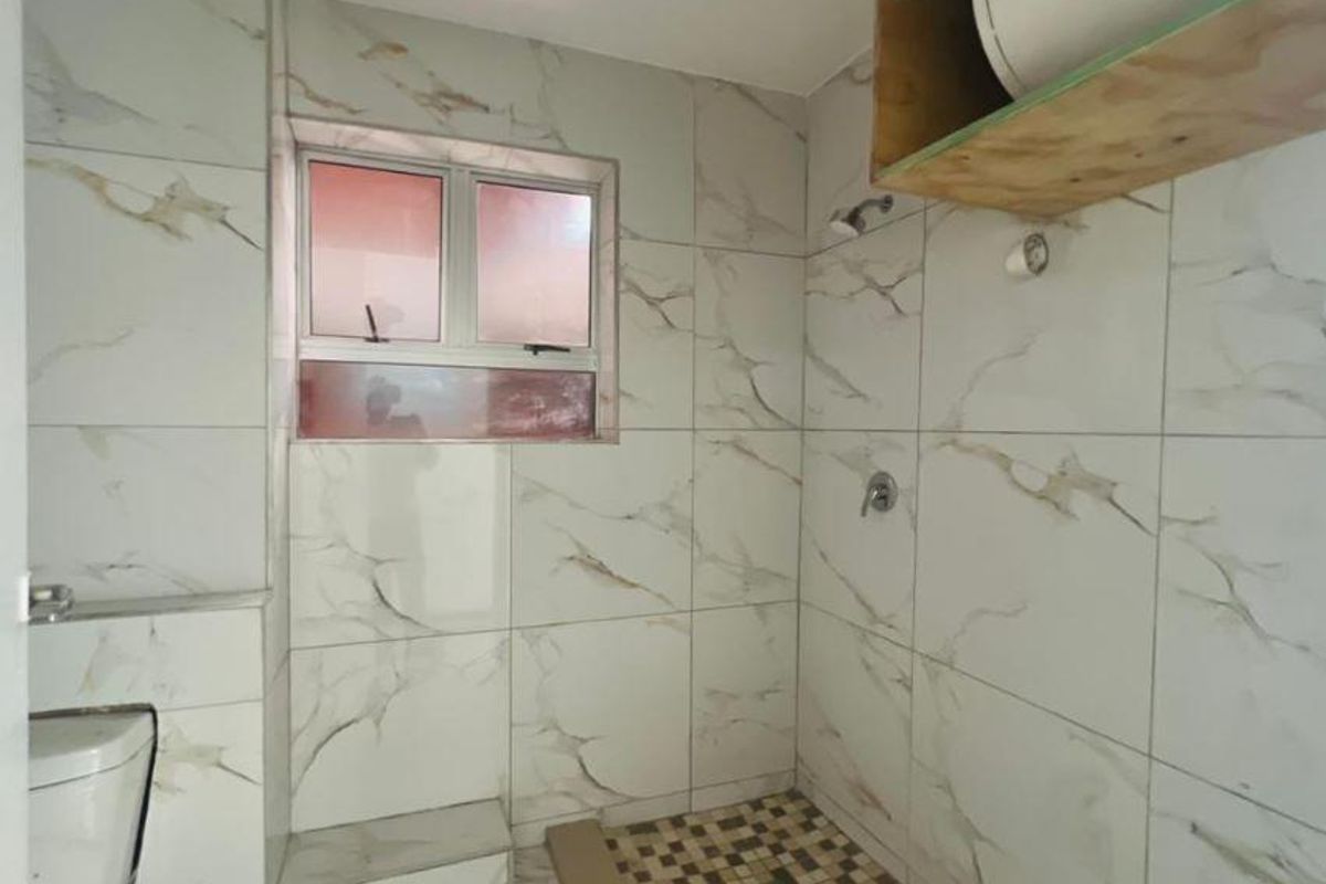 A bathroom featuring marble-effect wall tiles, a walk-in shower area with mosaic floor tiling, and an exposed water heater unit.