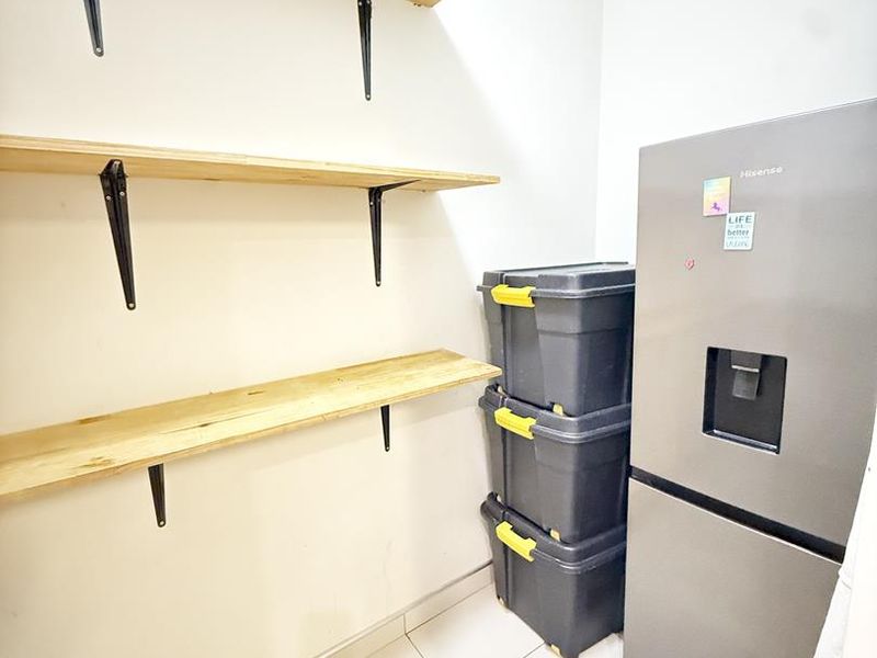 A functional scullery or pantry area featuring wall-mounted wooden shelving and tiled flooring, providing convenient additional storage space.
