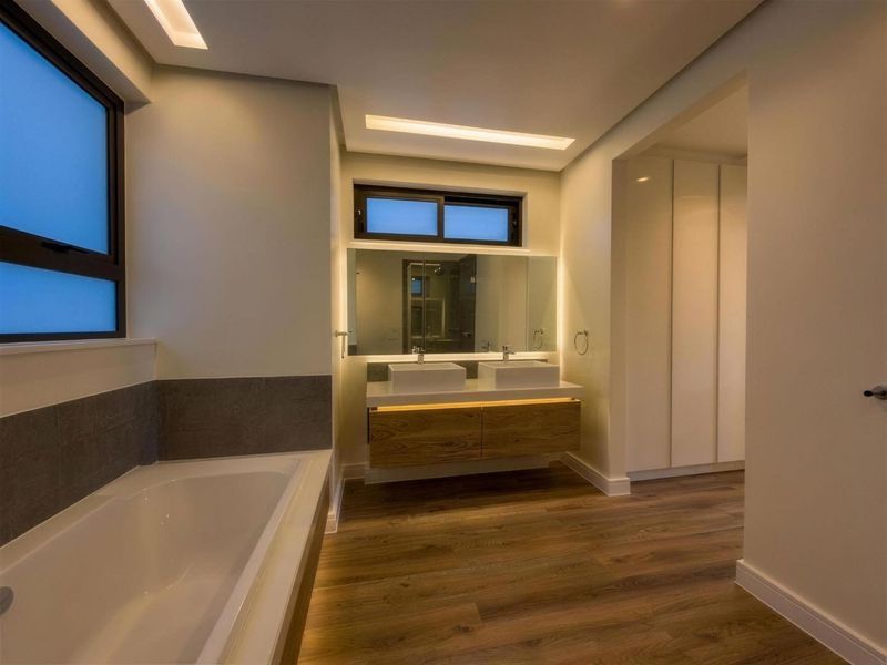 Modern bathroom featuring a double vanity with integrated lighting, a built-in bathtub, and sleek cabinetry, finished with high-quality laminate flooring.