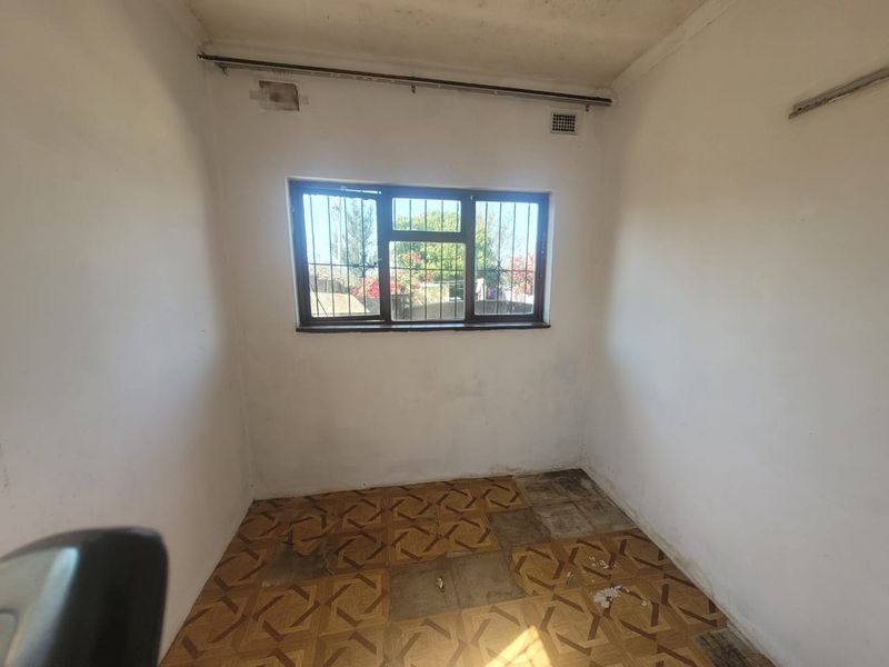An empty bedroom featuring original parquet flooring, security bars on the window, and ventilation bricks, requiring cosmetic updates and floor restoration.