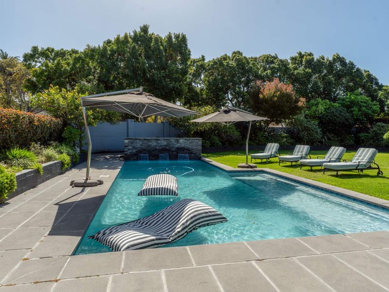 A well-maintained swimming pool area featuring a stone water feature, paved decking, and a lush landscaped garden setting.