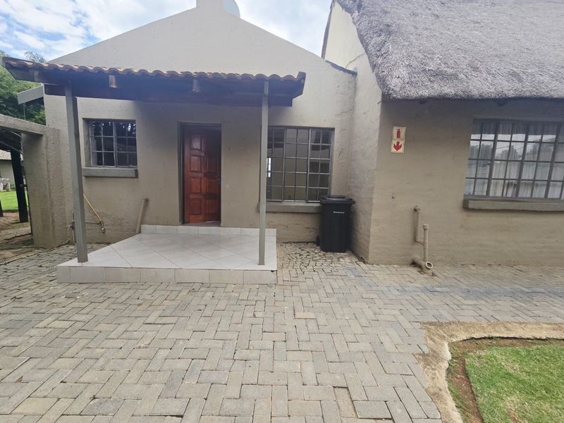 Front elevation of a cottage featuring a thatched roof, covered tiled porch, and paved driveway area.