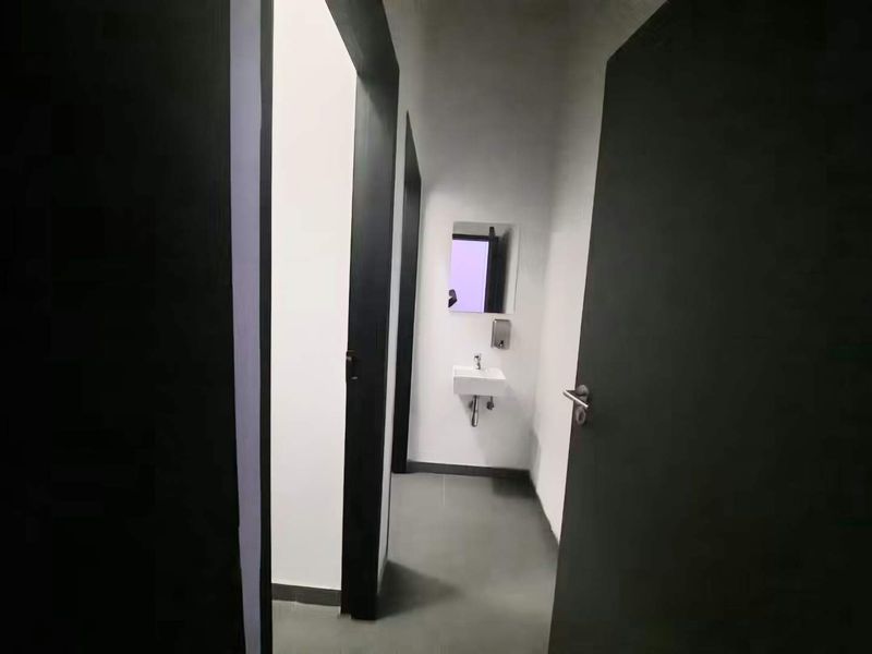 A minimalist bathroom featuring a wall-mounted basin, mirror, and soap dispenser with neutral tiled flooring and modern dark door frames.