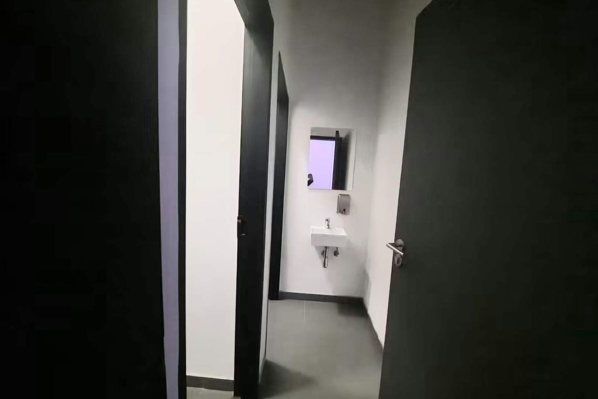 A minimalist bathroom featuring a wall-mounted basin, mirror, and soap dispenser with neutral tiled flooring and modern dark door frames.