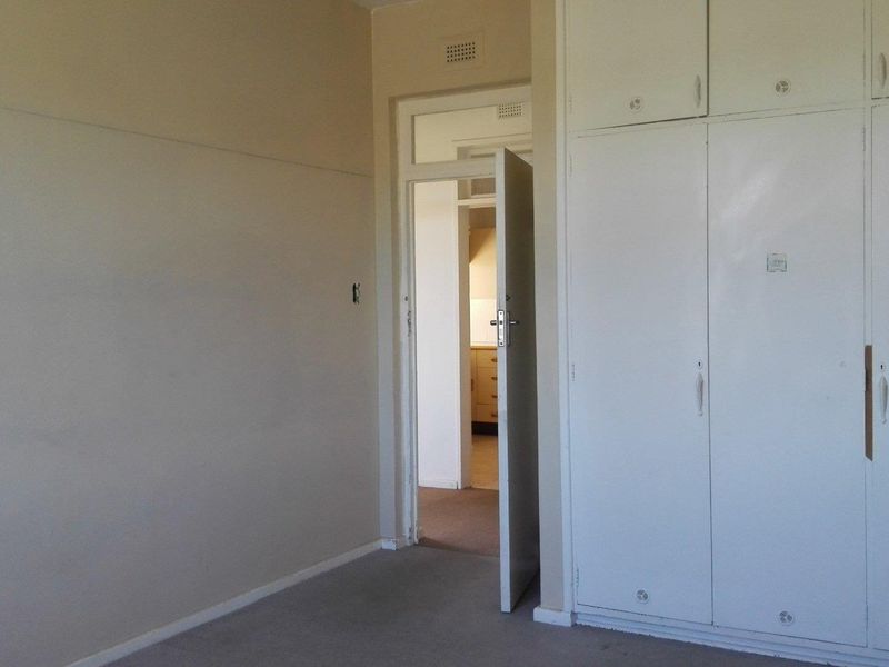 An empty bedroom featuring built-in cupboards and carpeted flooring, with a doorway leading to an adjacent room.