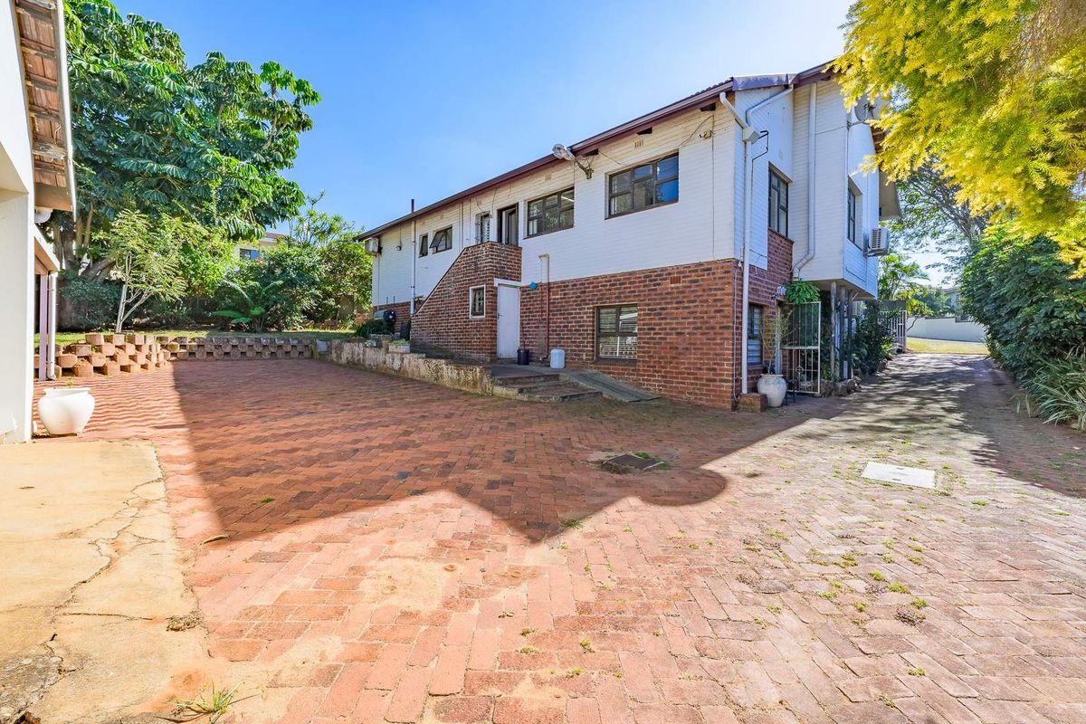 Rear exterior view of the property featuring a large brick-paved courtyard, retaining walls, and a two-story structure with brick and weatherboard finishes.