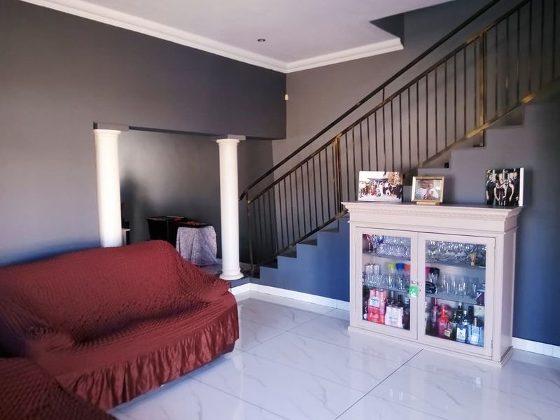 Living area featuring a staircase with metal balustrade, decorative columns, and modern tiled flooring with a neutral grey wall finish.