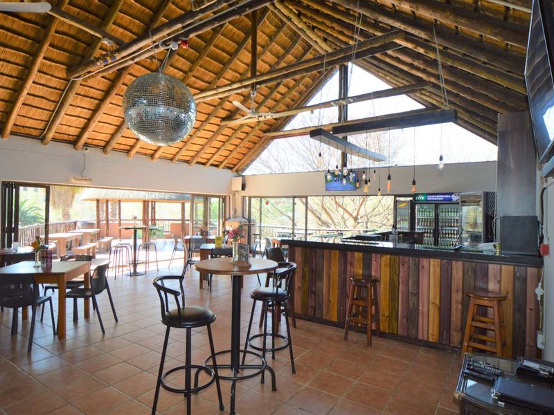 Spacious bar area featuring a high thatched roof with exposed timber trusses, tiled flooring, and large sliding glass doors opening to an outdoor patio.