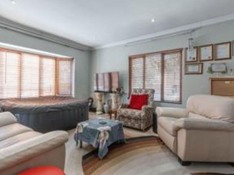 A spacious living room featuring a large bay window with venetian blinds, recessed downlighting, and coved cornicing, offering a bright and comfortable living space.