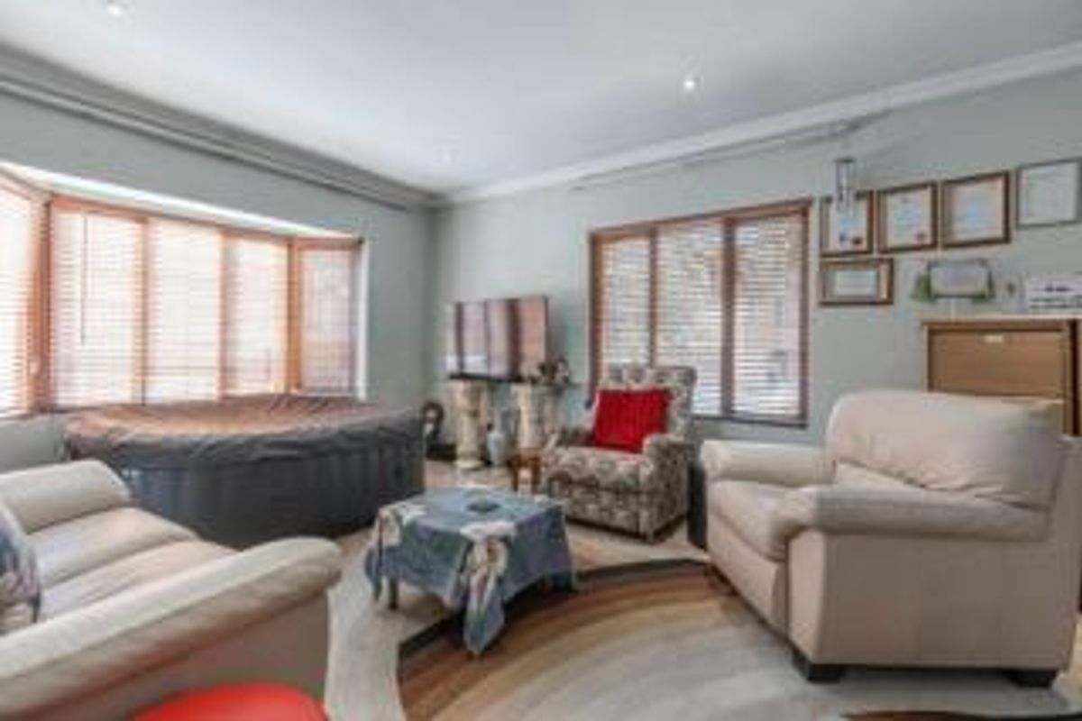 A spacious living room featuring a large bay window with venetian blinds, recessed downlighting, and coved cornicing, offering a bright and comfortable living space.