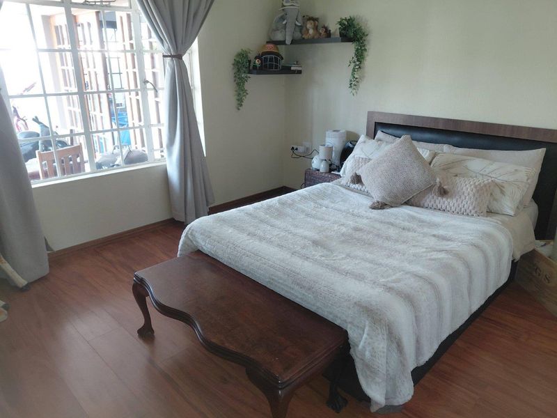 A cozy bedroom featuring laminate flooring, a large window allowing natural light, and built-in floating shelves for storage.