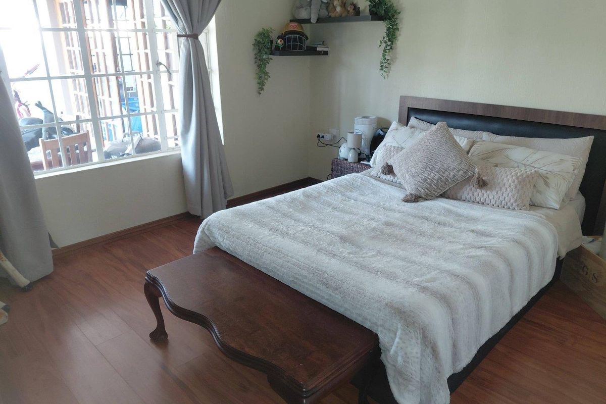 A cozy bedroom featuring laminate flooring, a large window allowing natural light, and built-in floating shelves for storage.