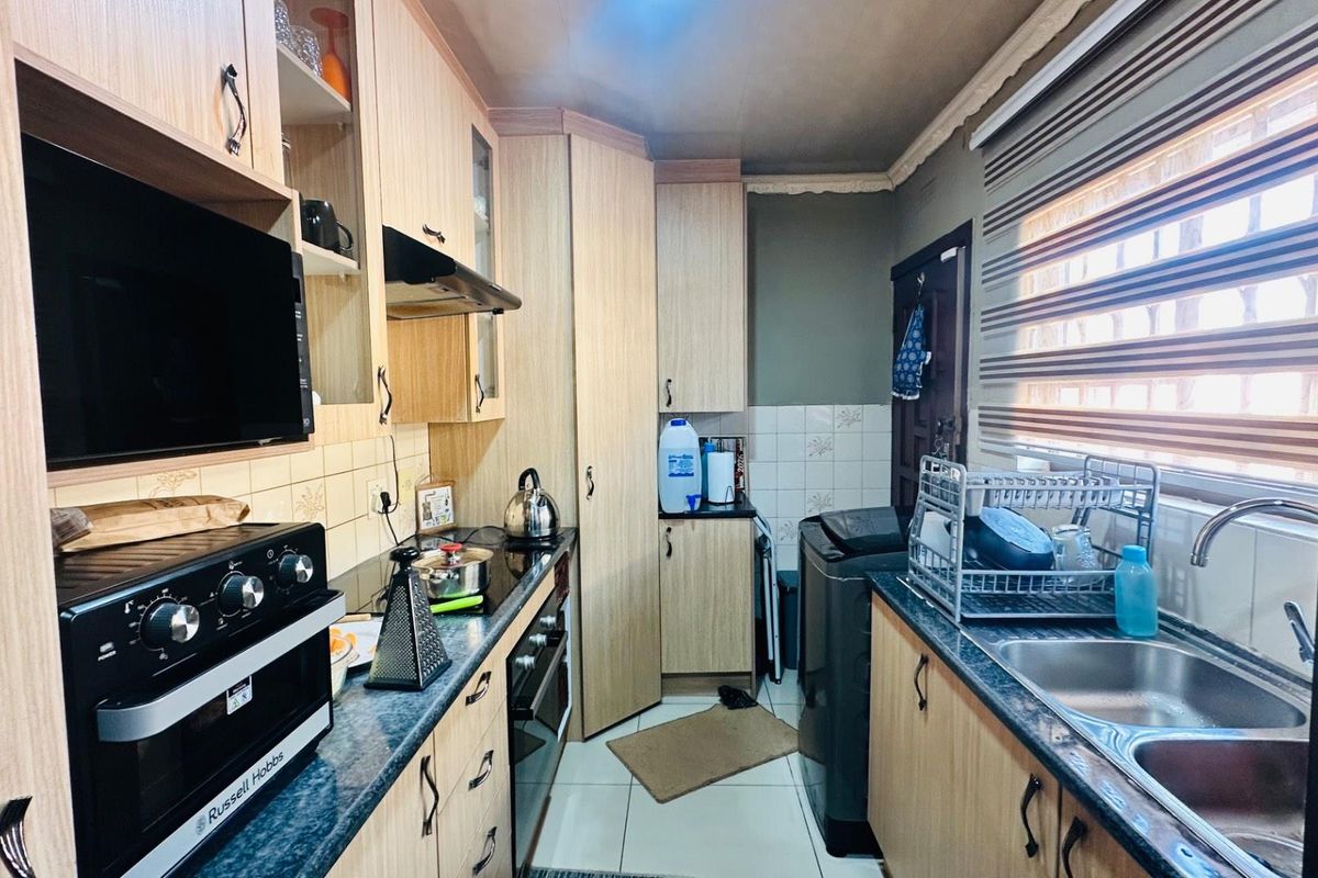A functional kitchen featuring light wood-finish cabinetry, laminate countertops, a double sink, and integrated extractor fan with tiled backsplash and flooring.