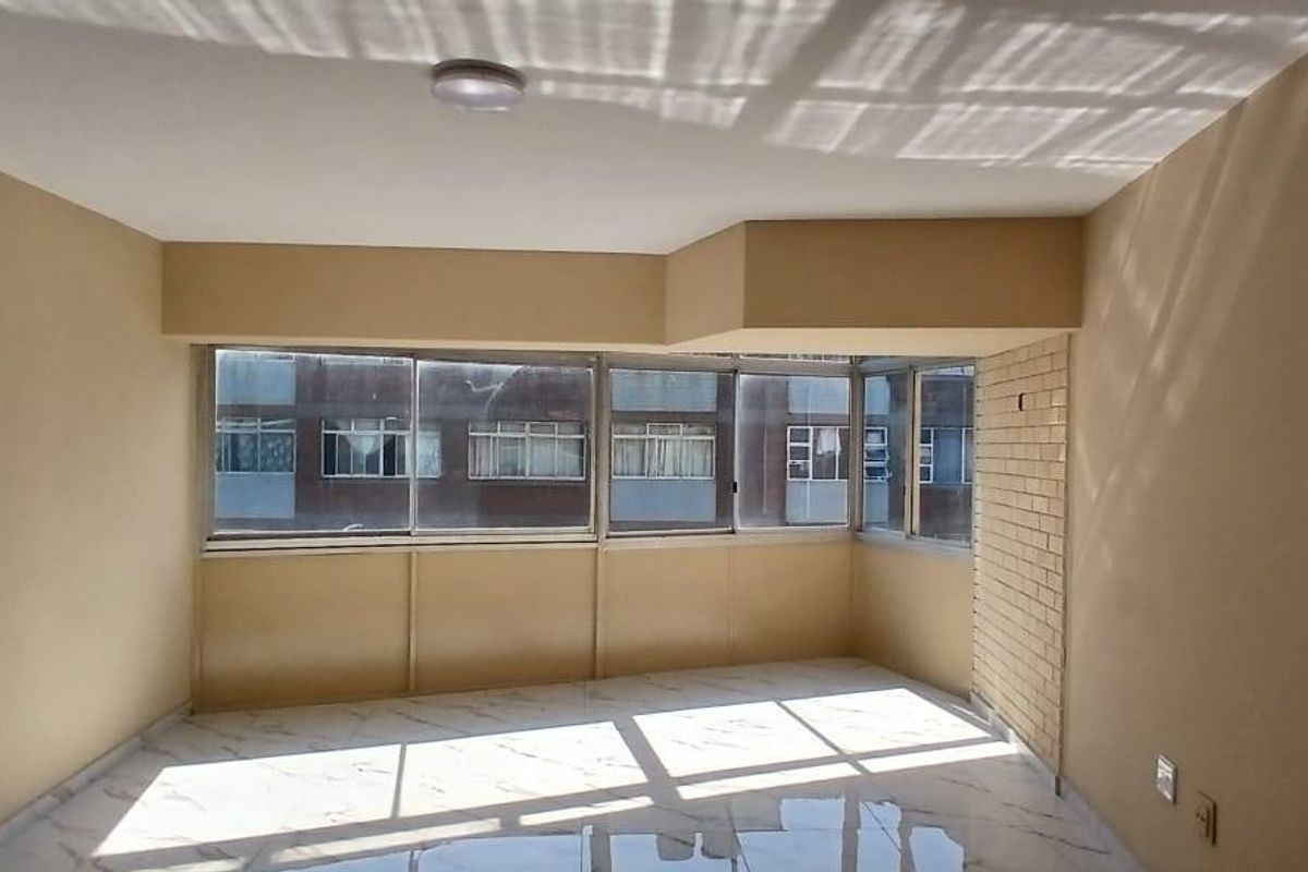 An empty living room featuring marble-look floor tiles, a brick accent wall, and large windows providing natural light.