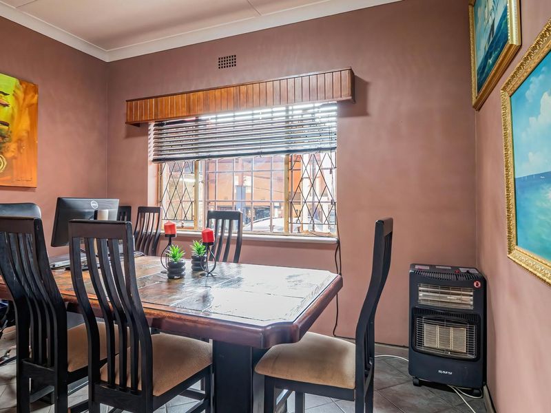 A dining room featuring tiled flooring, a window with security bars, and a timber pelmet, providing a functional space for meals or home office use.