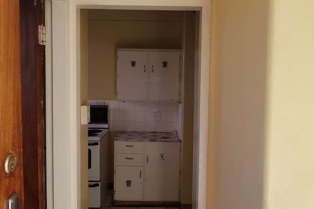 A compact kitchen featuring dated built-in cabinetry, tiled flooring, and a freestanding stove, offering potential for modernization and renovation.