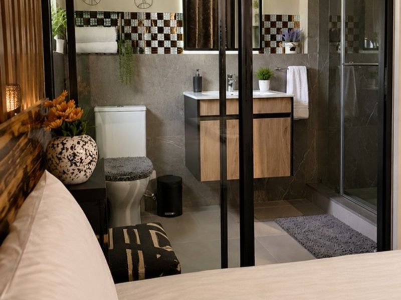 Modern en-suite bathroom featuring a floating vanity, glass-enclosed shower, and contemporary tiled finishes, conveniently accessible via a sleek sliding glass door from the bedroom.