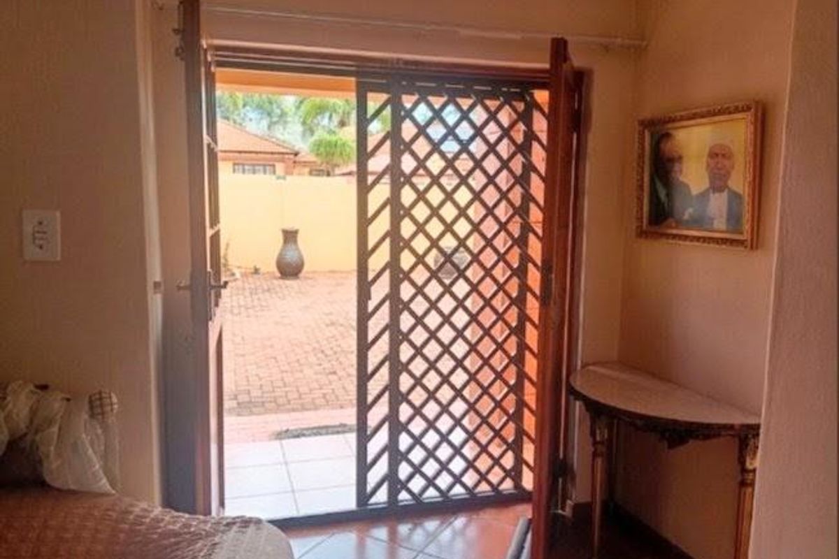 Living area featuring tiled flooring and double french doors opening onto a paved outdoor patio space with a security gate.