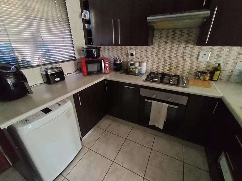 Compact kitchen featuring dark wood cabinetry, mosaic tile backsplash, gas hob, built-in oven, and extractor fan with tiled flooring.